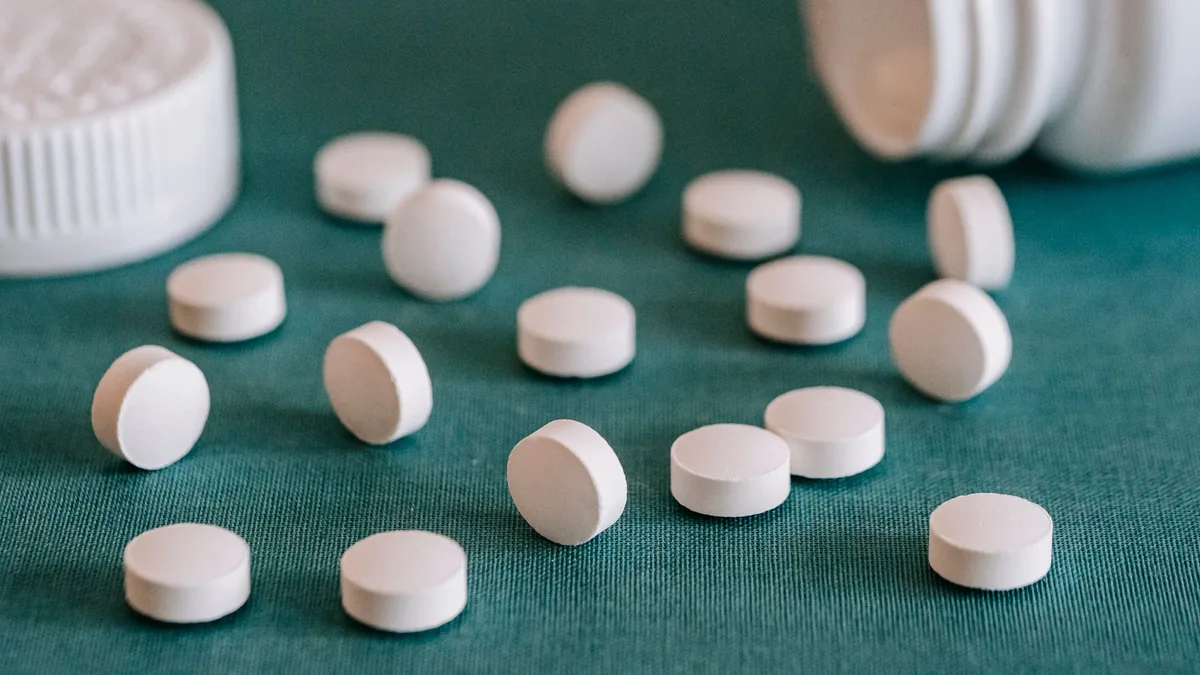 Comprimés blancs renversés d'un flacon, illustrant le quotidien pharmaceutique