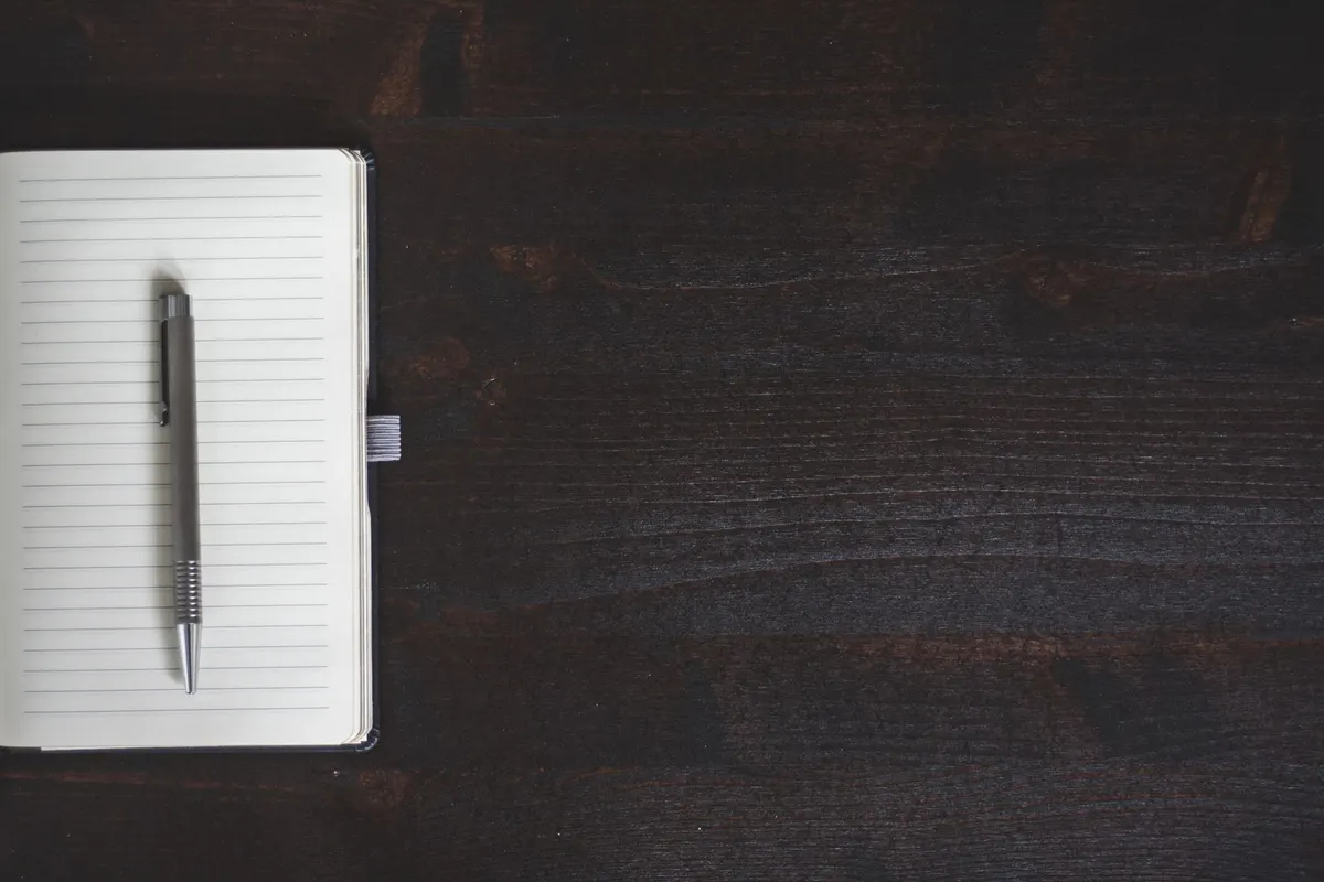 Stylo posé sur un carnet vierge sur un bureau en bois sombre, symbole de la rédaction d'un contrat individuel